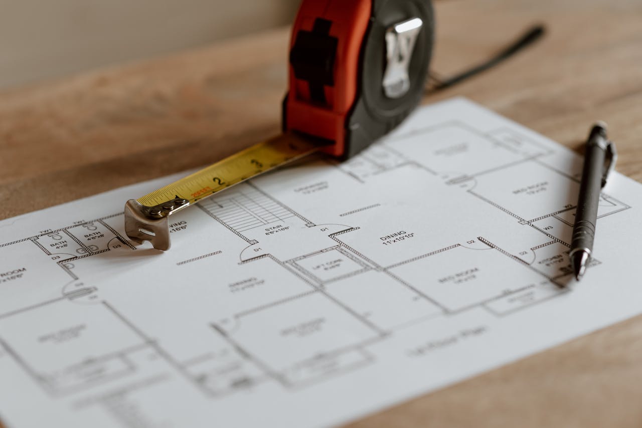 Close-up view of architectural blueprint with measuring tape and pen on a wooden table.