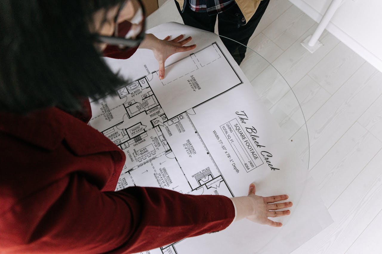 Top view of a woman reviewing detailed architectural blueprints on a glass table, discussing property details.